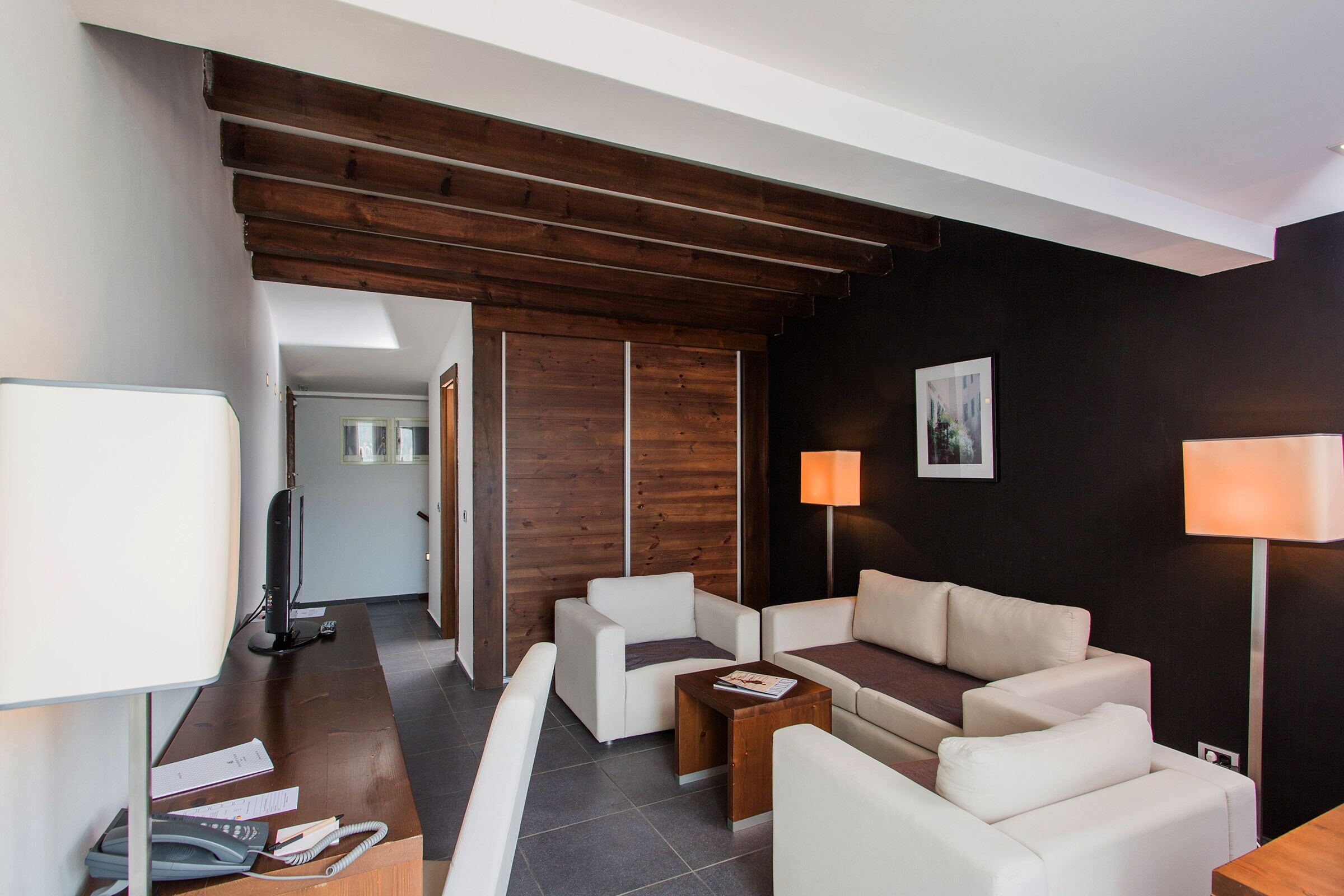 A modern living room with a wooden ceiling, white sofas, a coffee table, and a TV.