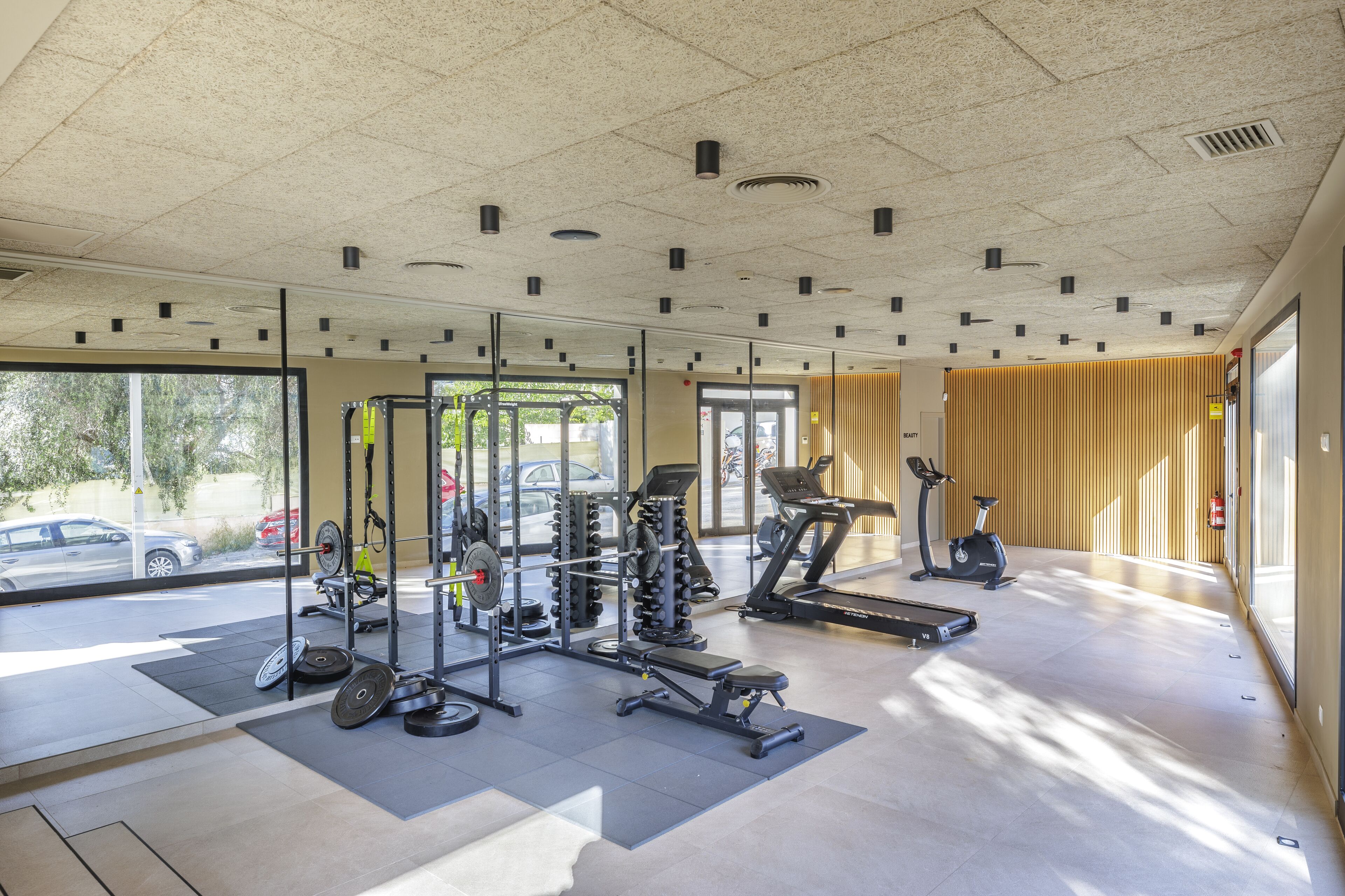A gym with various exercise equipment, large windows, and a view of the outside.