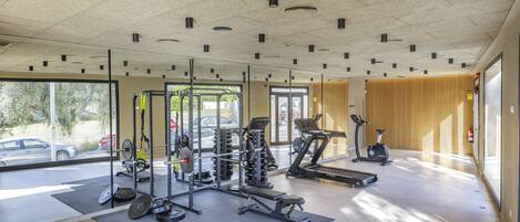 A gym with various exercise equipment, large windows, and a view of the outside.