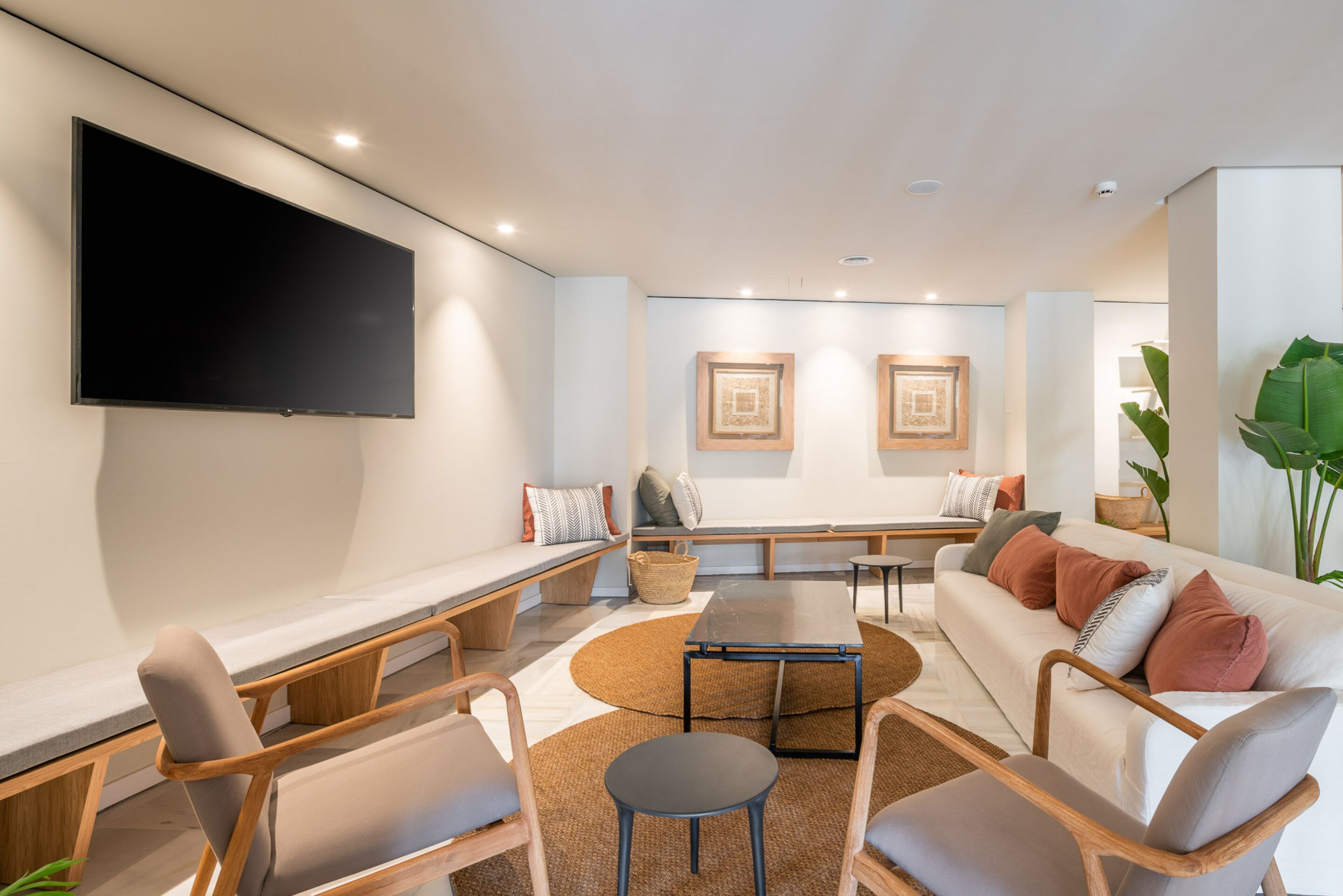 A modern living room with a flat-screen TV, a sofa, a coffee table, and a seating area with cushions and a woven rug.