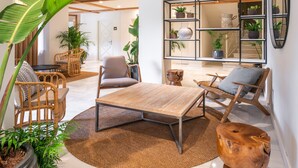 Un salón amplio con una mesa de centro de madera, sillas de mimbre y una planta grande en maceta.