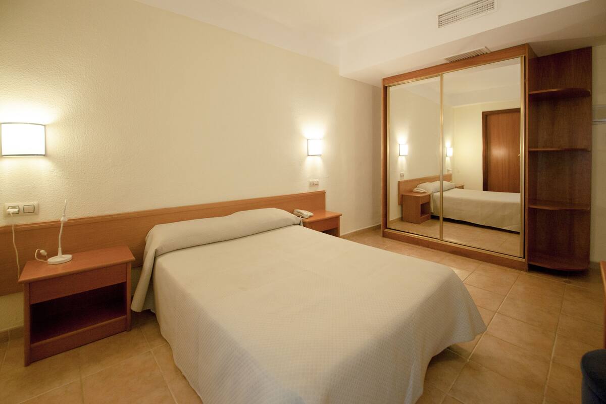 A hotel room with a bed, bedside table, nightstand, and a large mirror.
