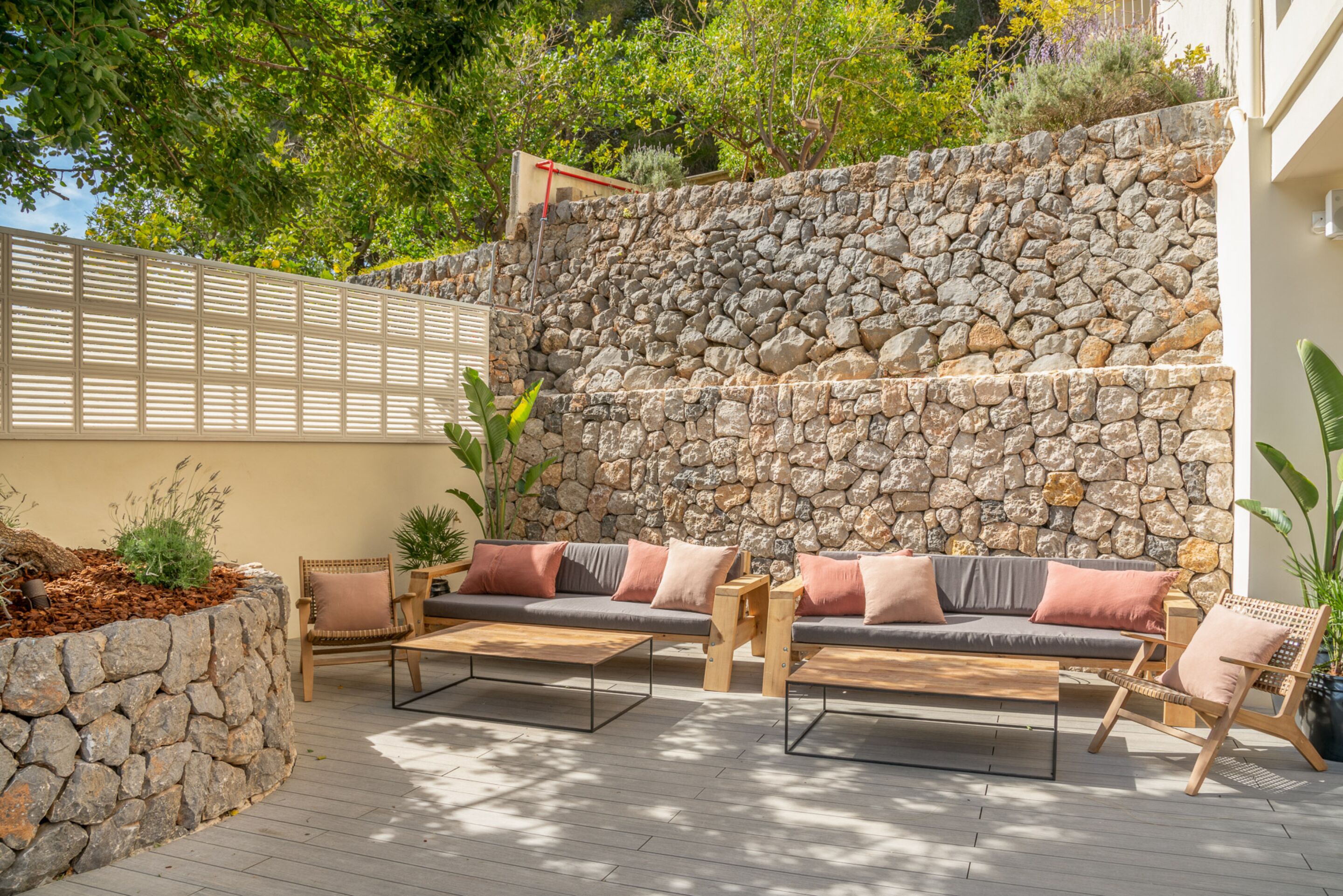 Un patio con un muro de piedra, un sofá de madera y dos sillas de madera.