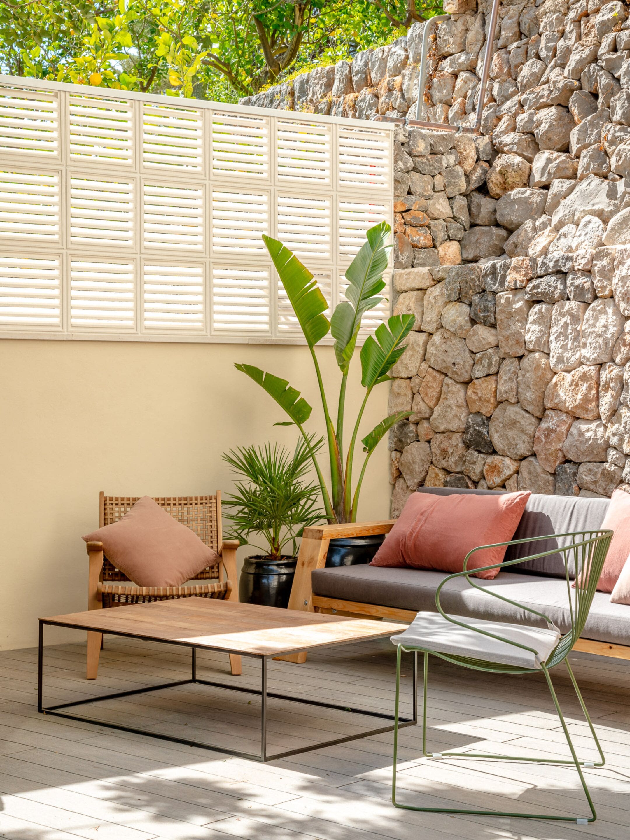 A patio area with a wooden table, two chairs, a sofa, and a large plant.