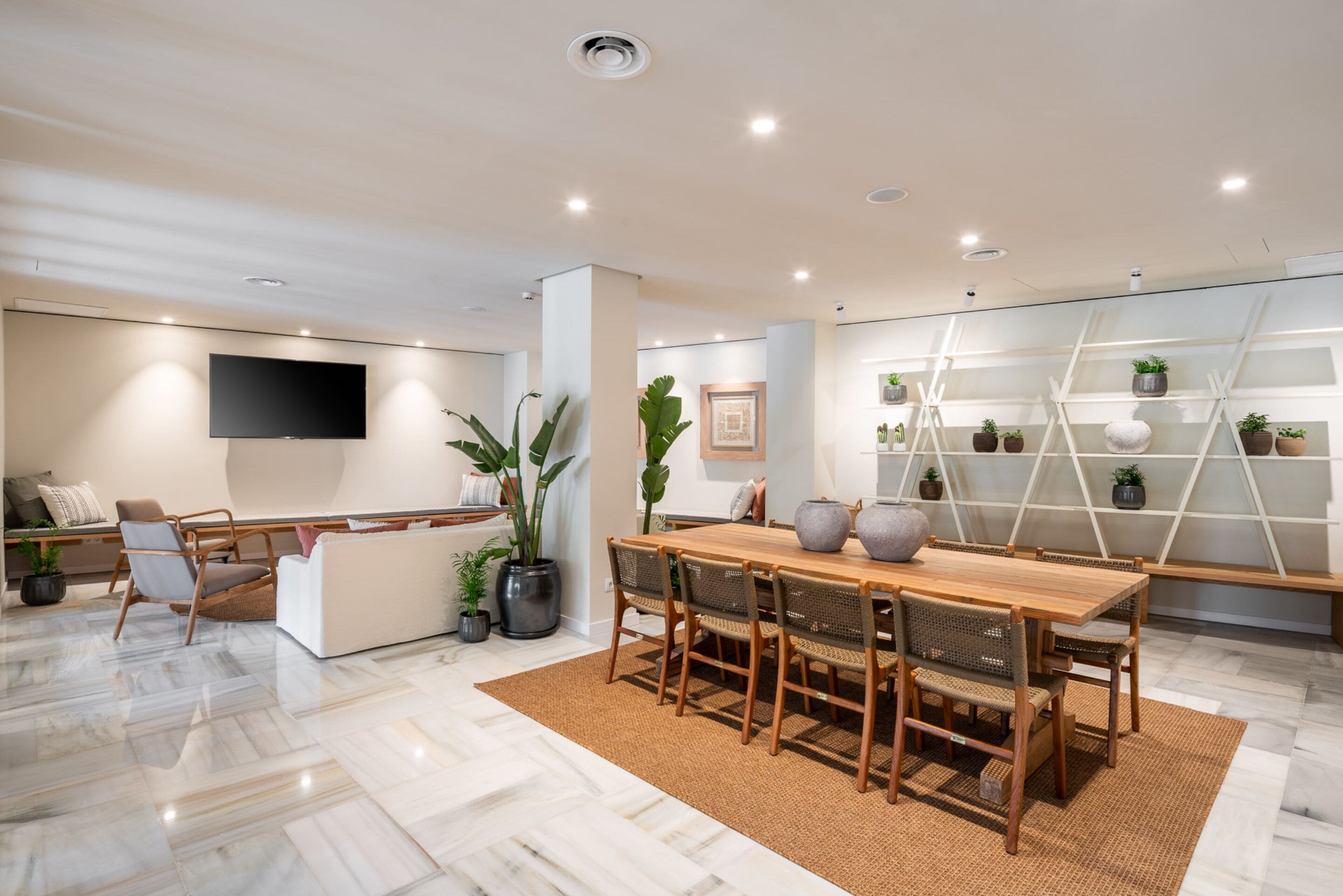 A modern living room with a wooden dining table, comfortable seating, a flat-screen TV, and a decorative plant wall.