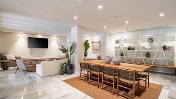 A modern living room with a wooden dining table, comfortable seating, a flat-screen TV, and a decorative plant wall.