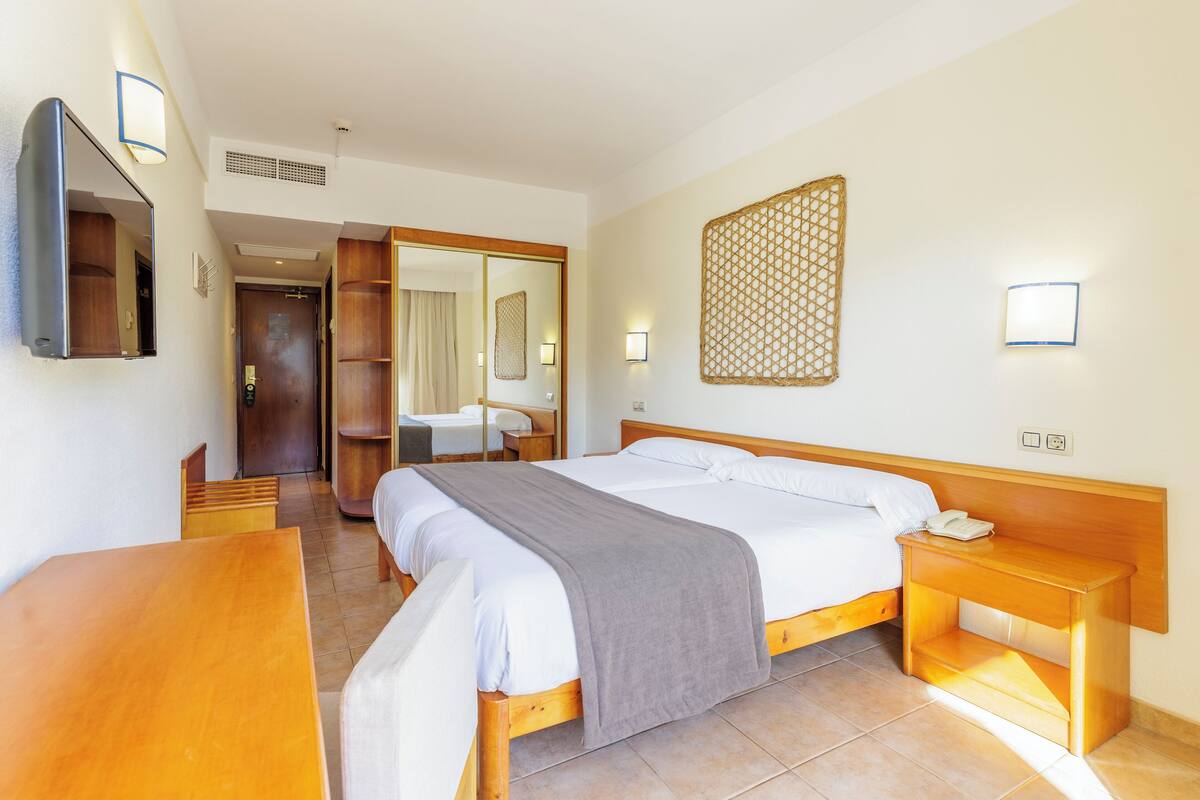 A hotel room with a large bed, bedside tables, a desk, a mirror, and a bathroom visible through an open door.
