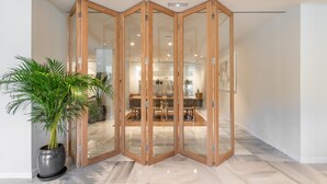 Habitación con separador de vidrio de madera, una planta en maceta y una zona de comedor al fondo.