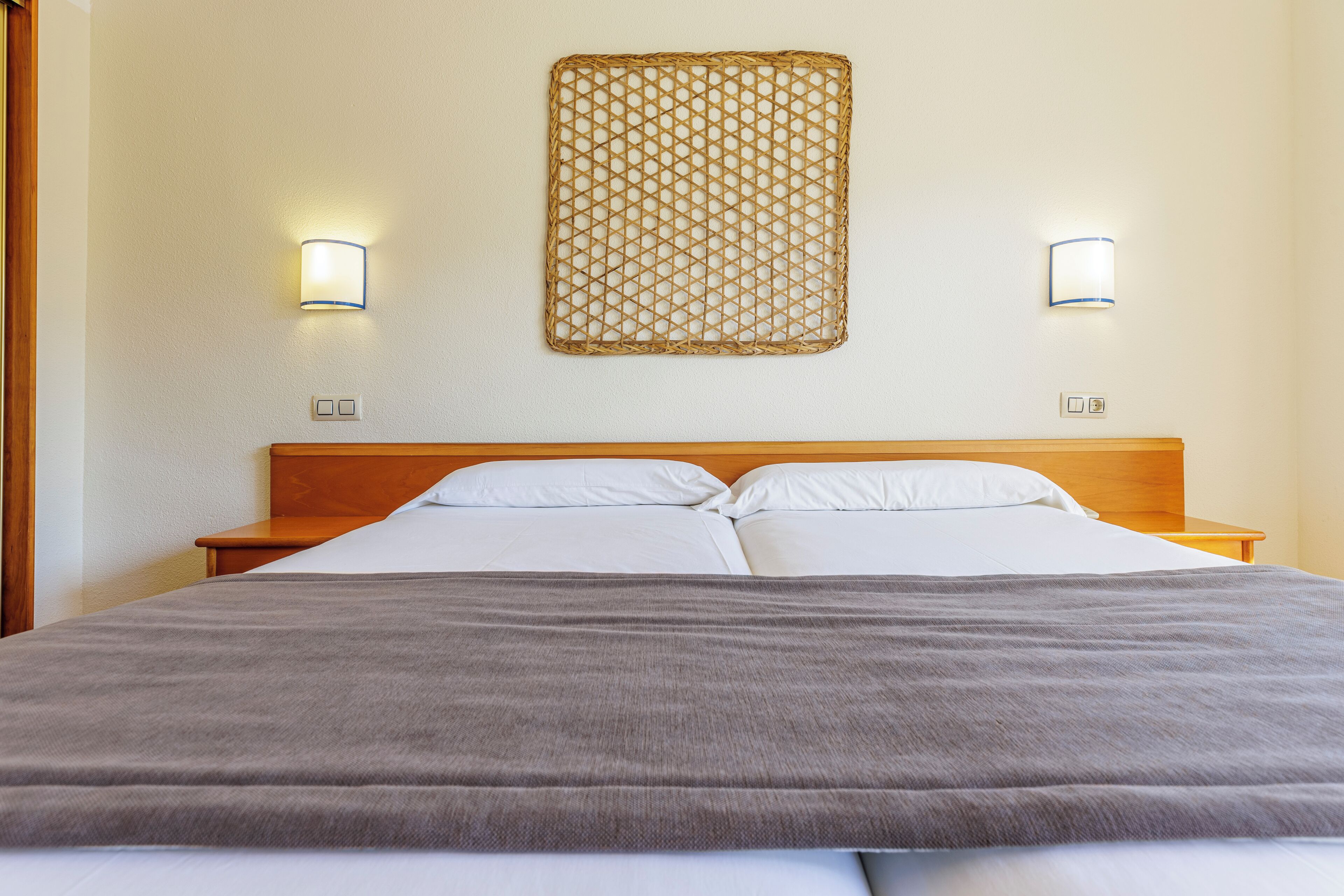 A hotel room with a bed, two bedside tables, a wooden headboard, and a wall-mounted decorative panel.
