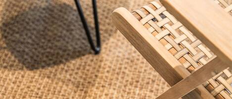 A round wooden table with metal legs and a woven chair with a wooden frame and woven seat.