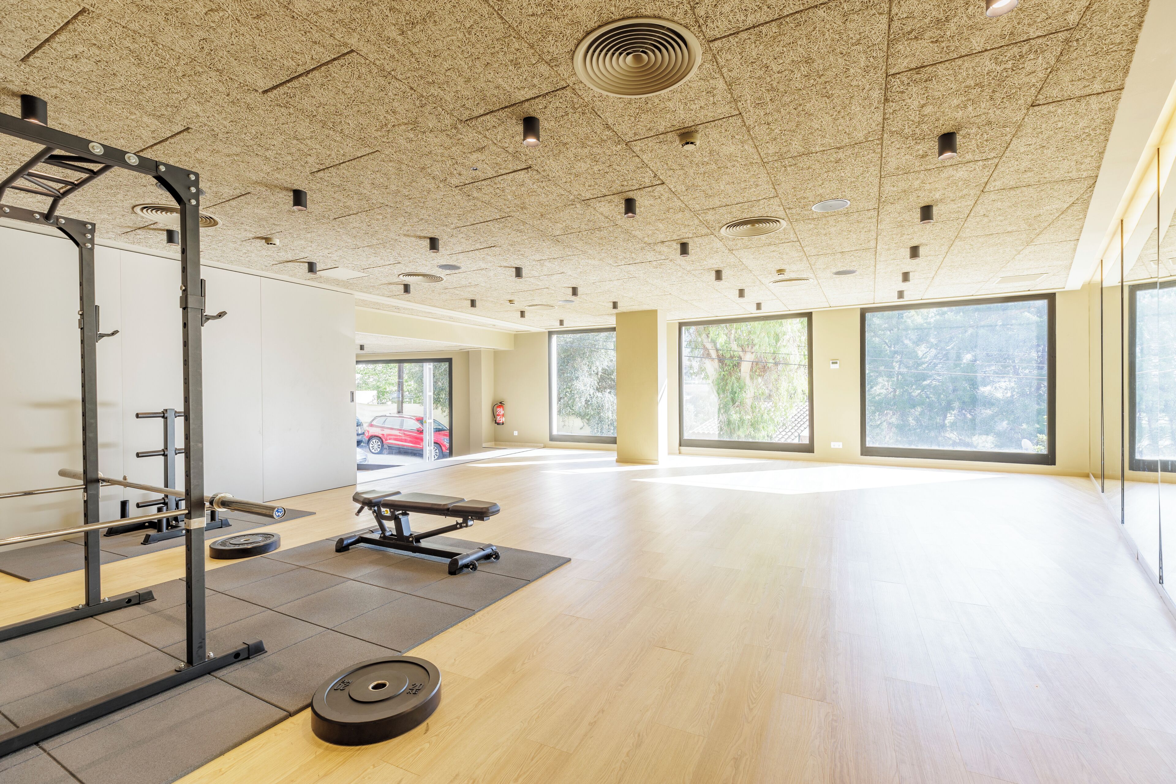 Un gimnasio amplio con suelo de madera, equipamiento de levantamiento de pesas y grandes ventanales que dejan entrar luz natural.