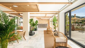 Un espacio interior amplio con techo de madera, ventanas grandes y plantas en macetas.