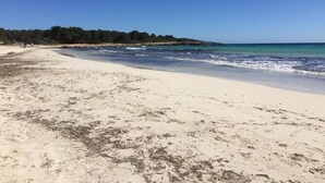 A beach with clear blue water, sandy shore, and a forested area in the background. - BJ Playa Blanca (Sant Llorenc des Cardassar)