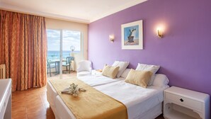 A hotel room with a bed, a nightstand, a chair, a table, and a view of the ocean through a sliding door. - BJ Playa Blanca (Sant Llorenc des Cardassar)