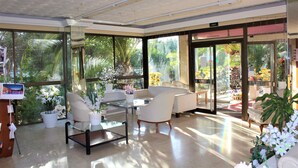 A spacious indoor area with large windows, a glass table, white chairs, and potted plants. - BJ Playa Blanca (Sant Llorenc des Cardassar)