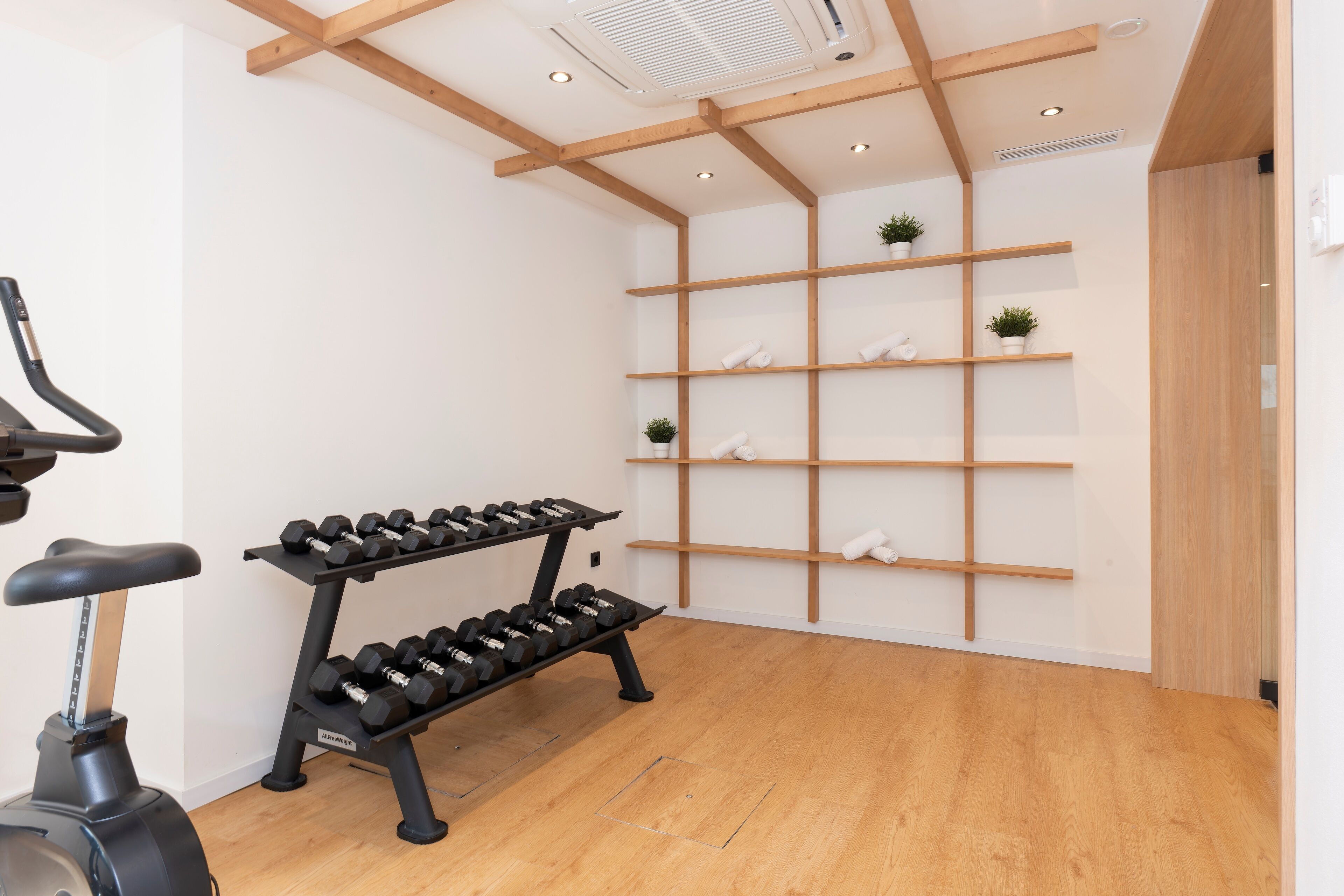 Un gimnasio con suelos de madera, una bicicleta estática y mancuernas en estanterías.