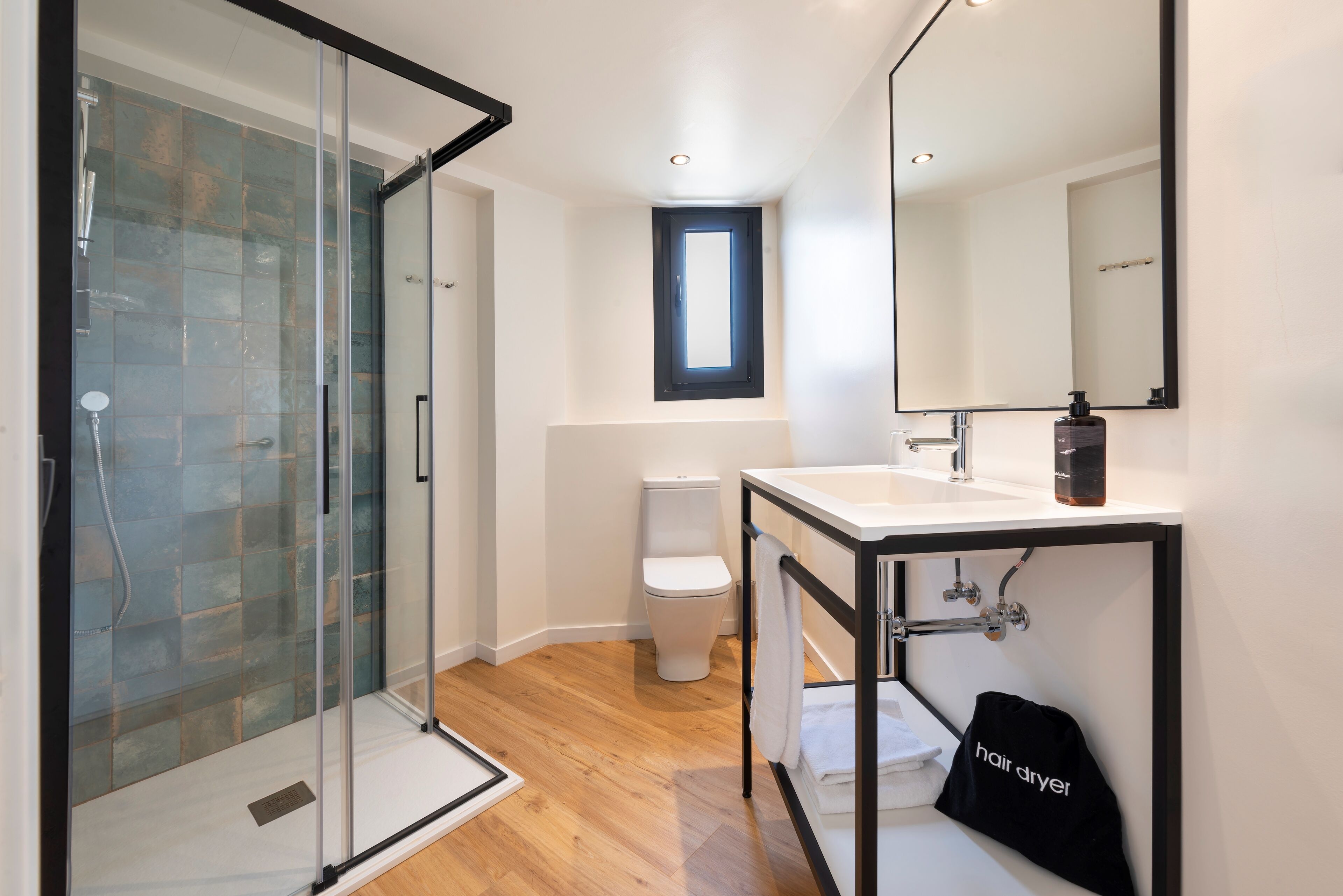 Un baño moderno con cabina de ducha de vidrio, inodoro blanco y lavamanos con toallero negro.