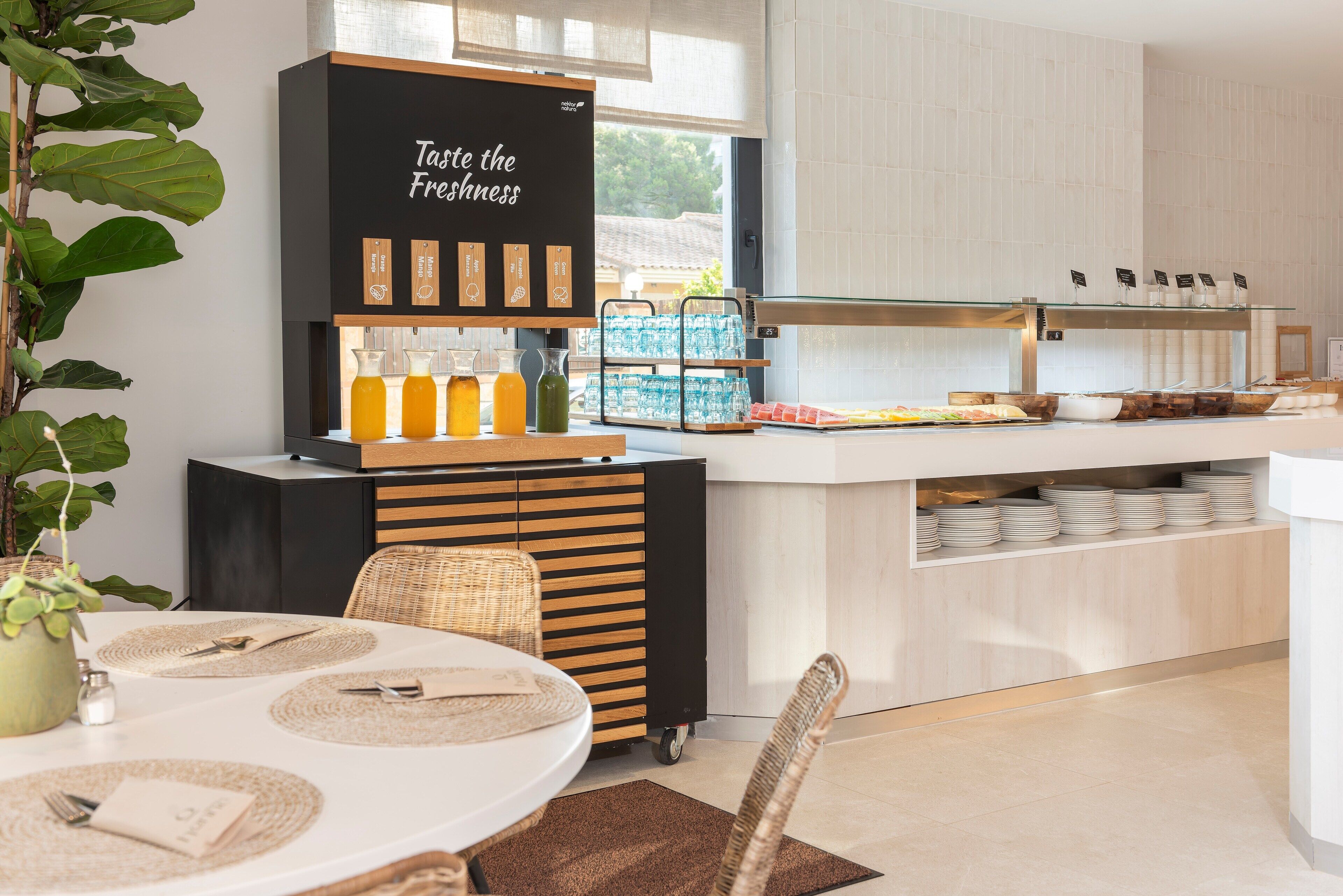 A modern kitchen with a blackboard sign, a buffet area with water bottles, and a dining table set with placemats and cutlery.