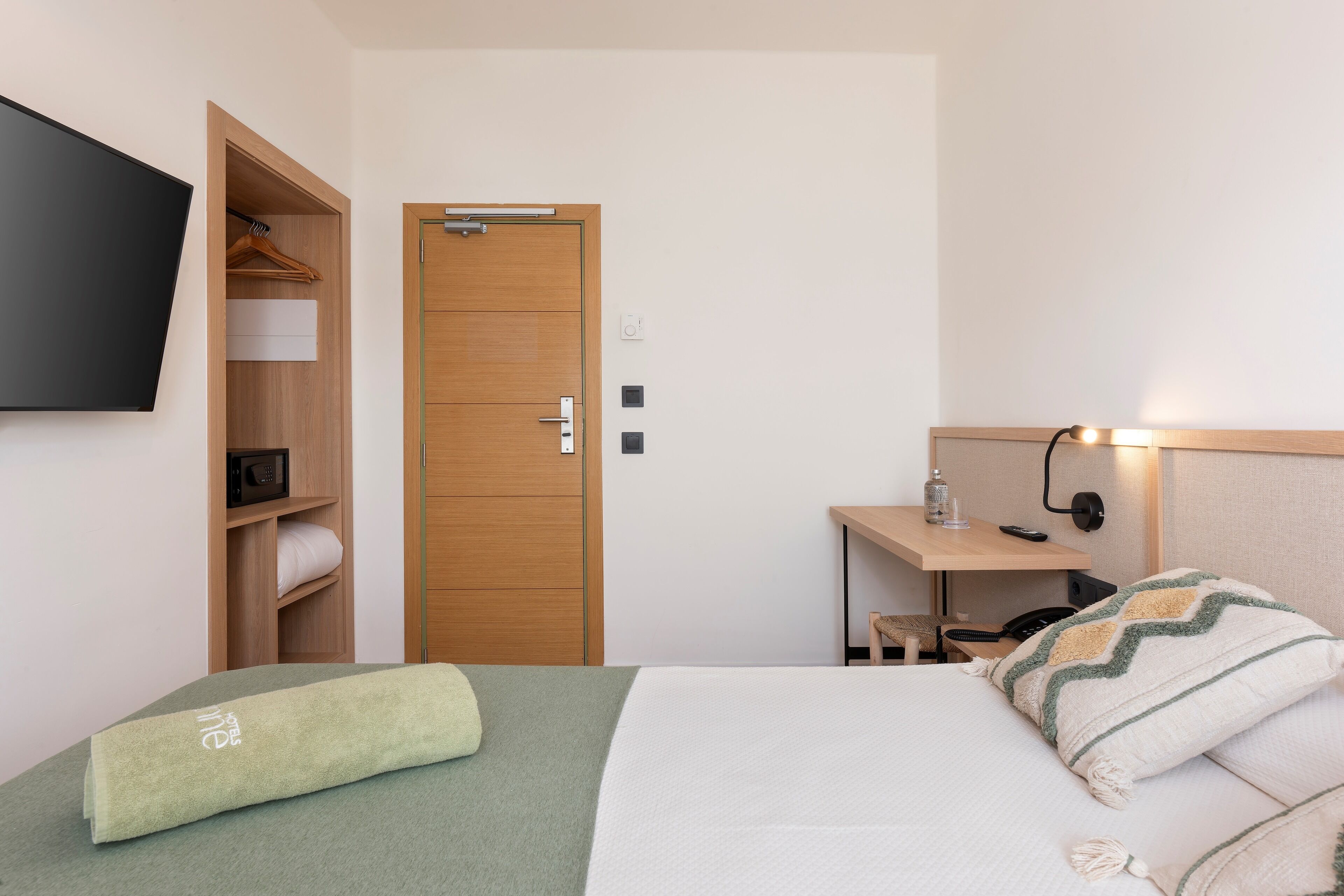 Habitación de hotel con cama, armario de madera, escritorio con lámpara y televisor montado en la pared.