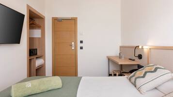 Habitación de hotel con cama, armario de madera, escritorio con lámpara y televisor montado en la pared.