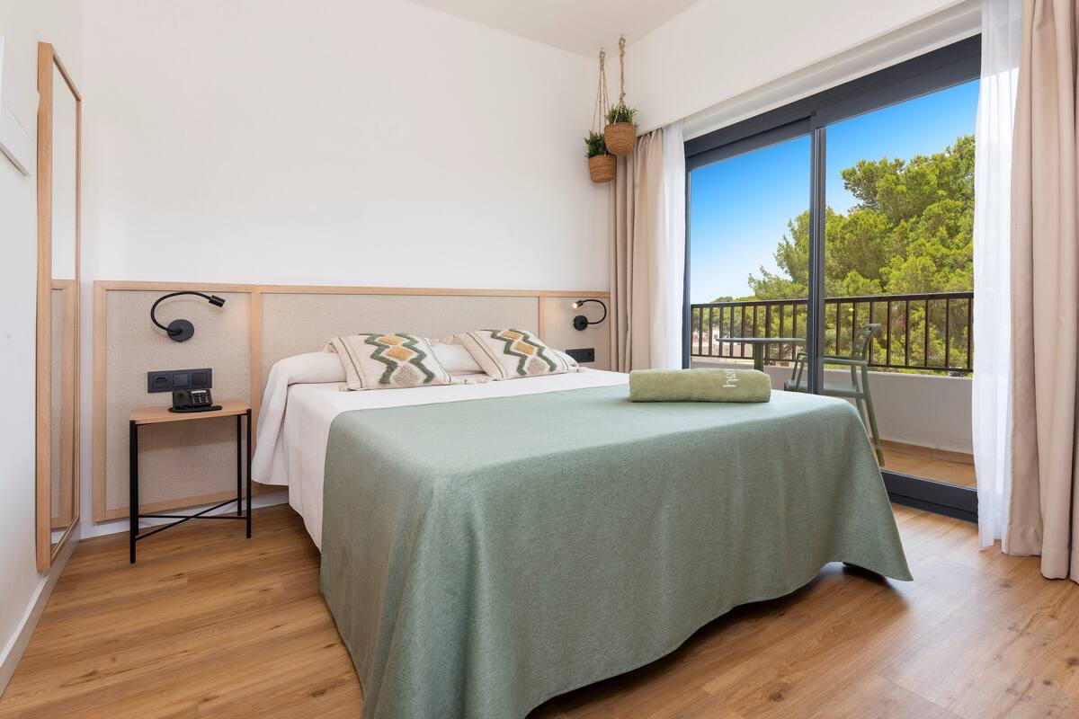 Een slaapkamer met een bed, nachtkastje en uitzicht op een balkon.