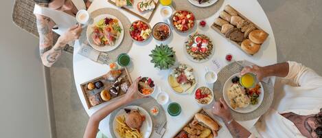 Una mesa redonda con diversos platos y bebidas, rodeada de gente.