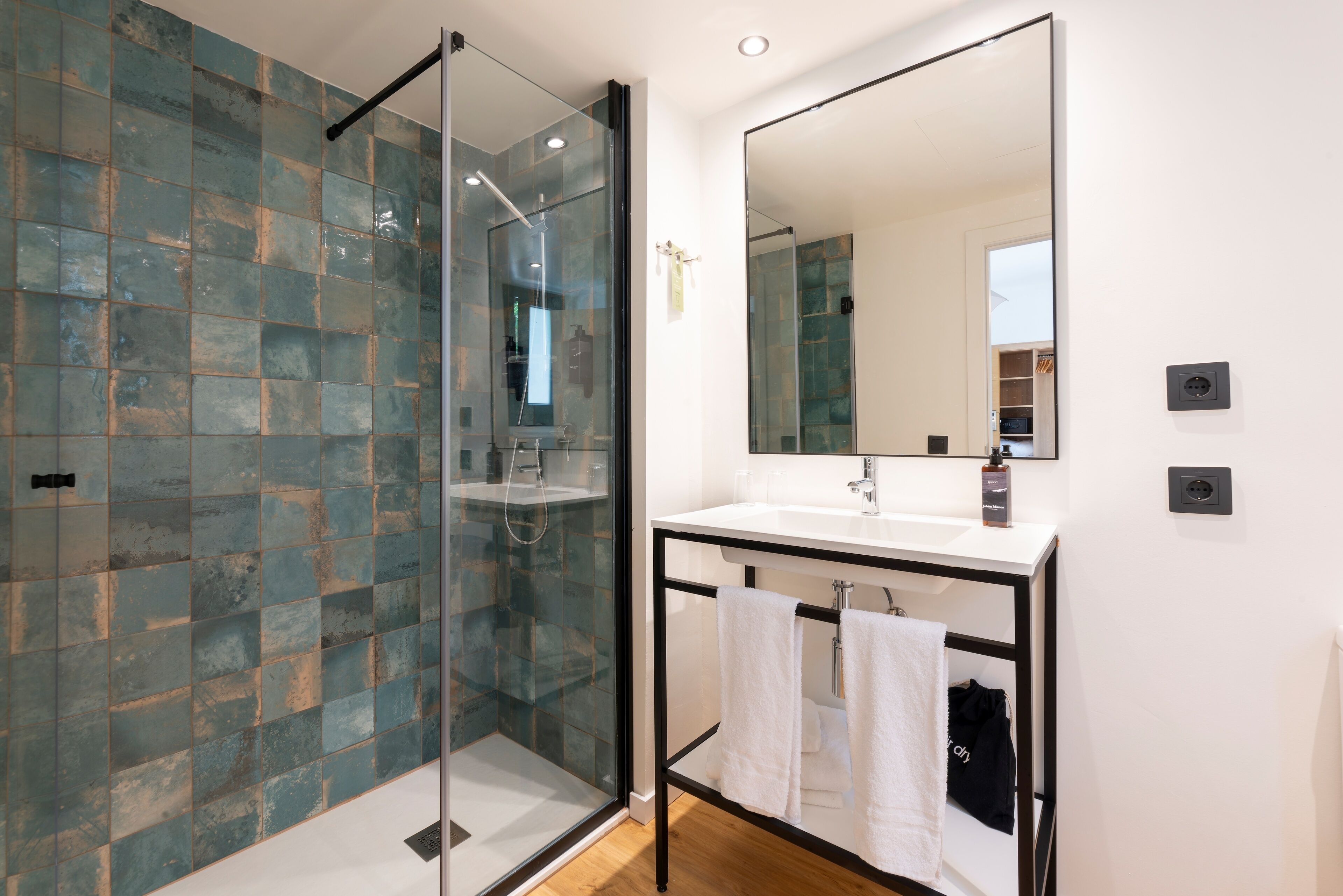 A modern bathroom with a glass shower enclosure, a white sink with a black frame, and a large mirror.