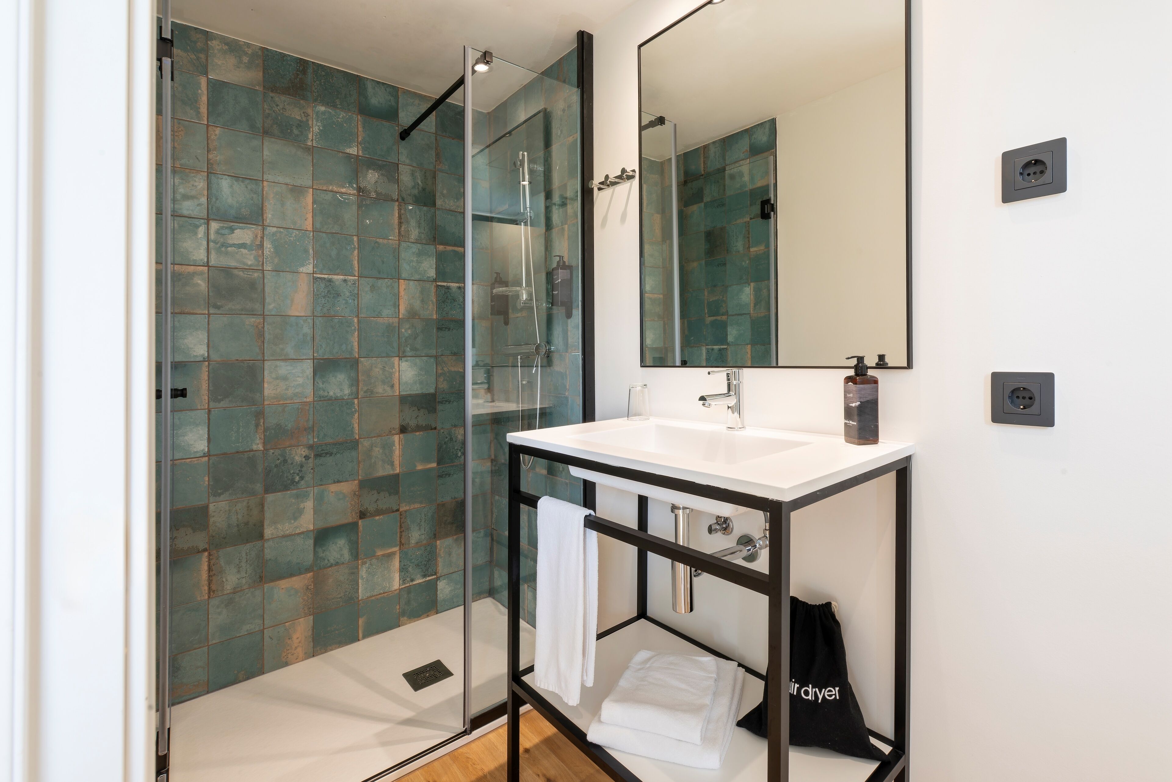 Un baño moderno con ducha de vidrio, un lavamanos blanco y un espejo grande.
