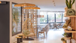 Un interior moderno con una zona de estar que incluye una silla de mimbre, mesas de madera y un separador decorativo.