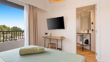 Une chambre d’hôtel comprenant un lit, une télévision, un bureau en bois, une chaise, une salle de bain avec un miroir et un balcon avec une balustrade.