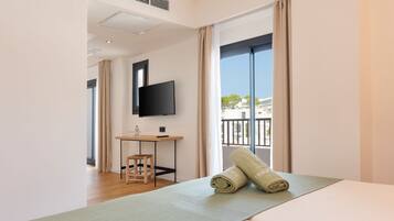 A modern hotel room with a large bed, a small desk, a television, and a view of the city through large windows.