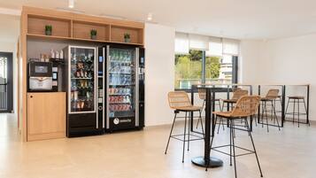 Un área de cocina moderna con refrigerador, máquina expendedora y comedor con taburetes de bar.