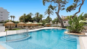Una piscina con sillas de descanso y sombrillas, rodeada de palmeras y edificios.