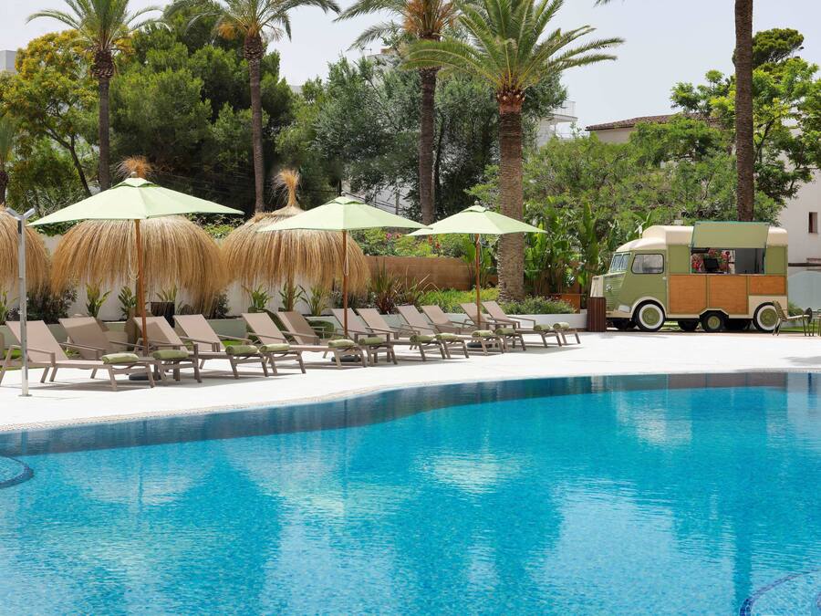 Piscina com espreguiçadeiras e guarda-sóis, um food truck e palmeiras.
