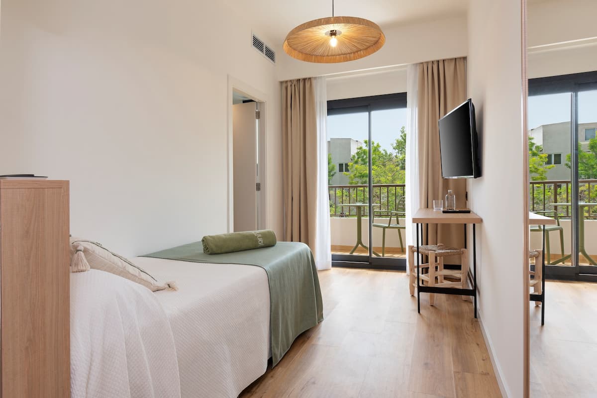 Een hotelkamer met een bed, een bureau met stoel, een televisie en een balkon met tafel en stoelen.
