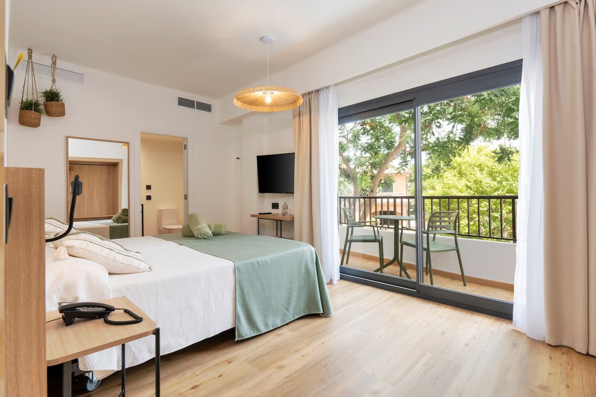 Een moderne hotelkamer met een bed, bureau, stoel, televisie en een balkon met uitzicht op groen.