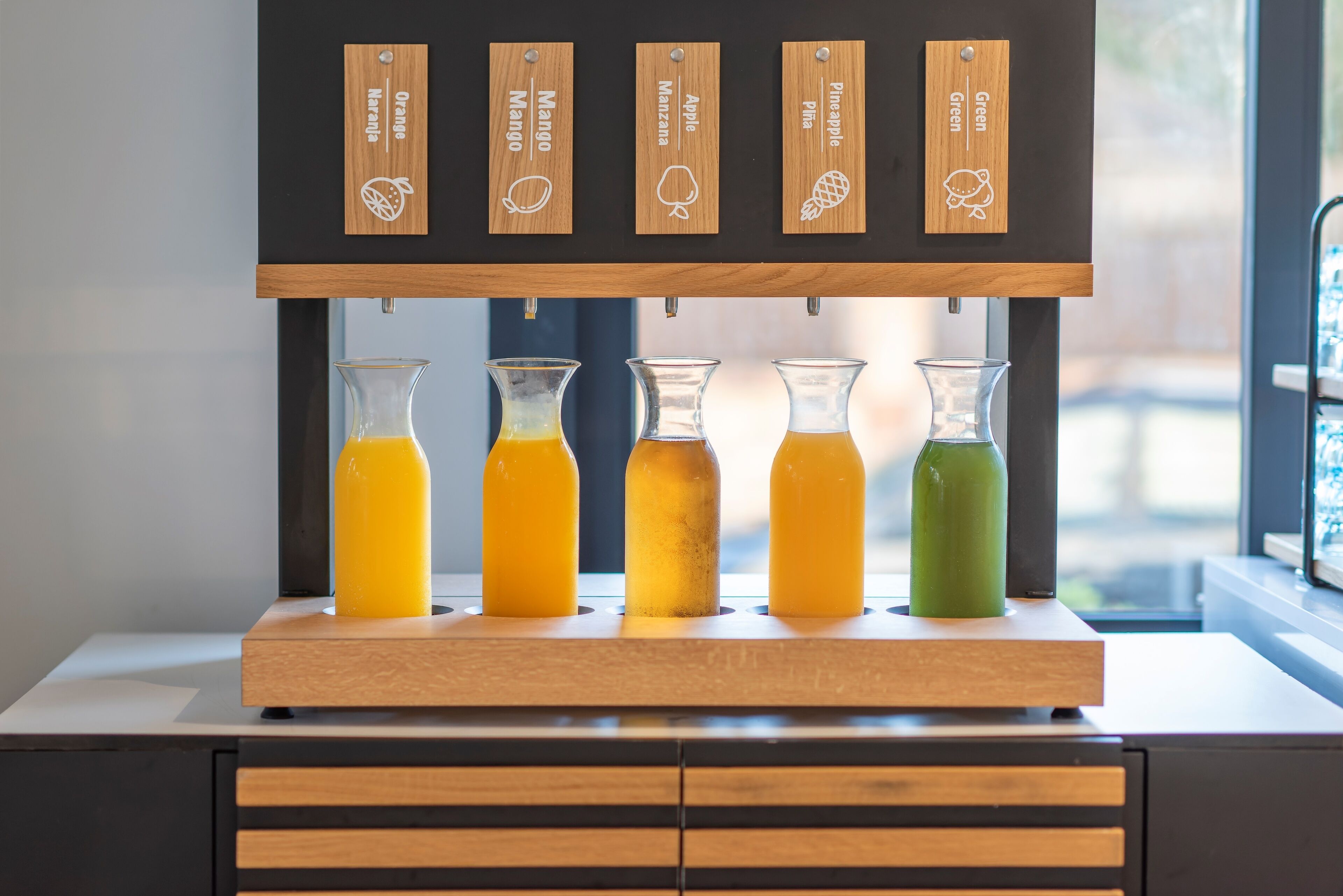 Un bar de zumos con etiquetas de madera para distintos jugos de fruta y cinco botellas de vidrio con jugo.