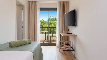 Habitación de hotel con cama, televisión, una mesita y balcón con vistas a árboles.