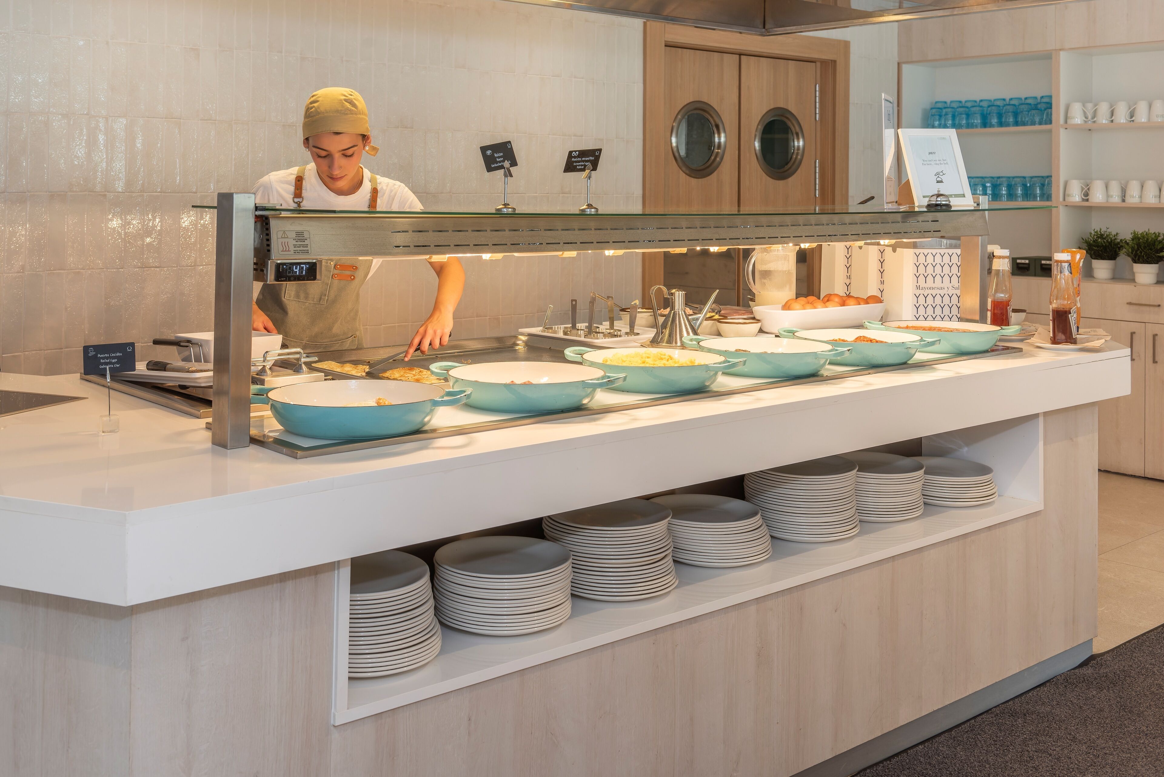 A buffet setup with multiple serving stations, a person serving food, and a variety of dishes and utensils.
