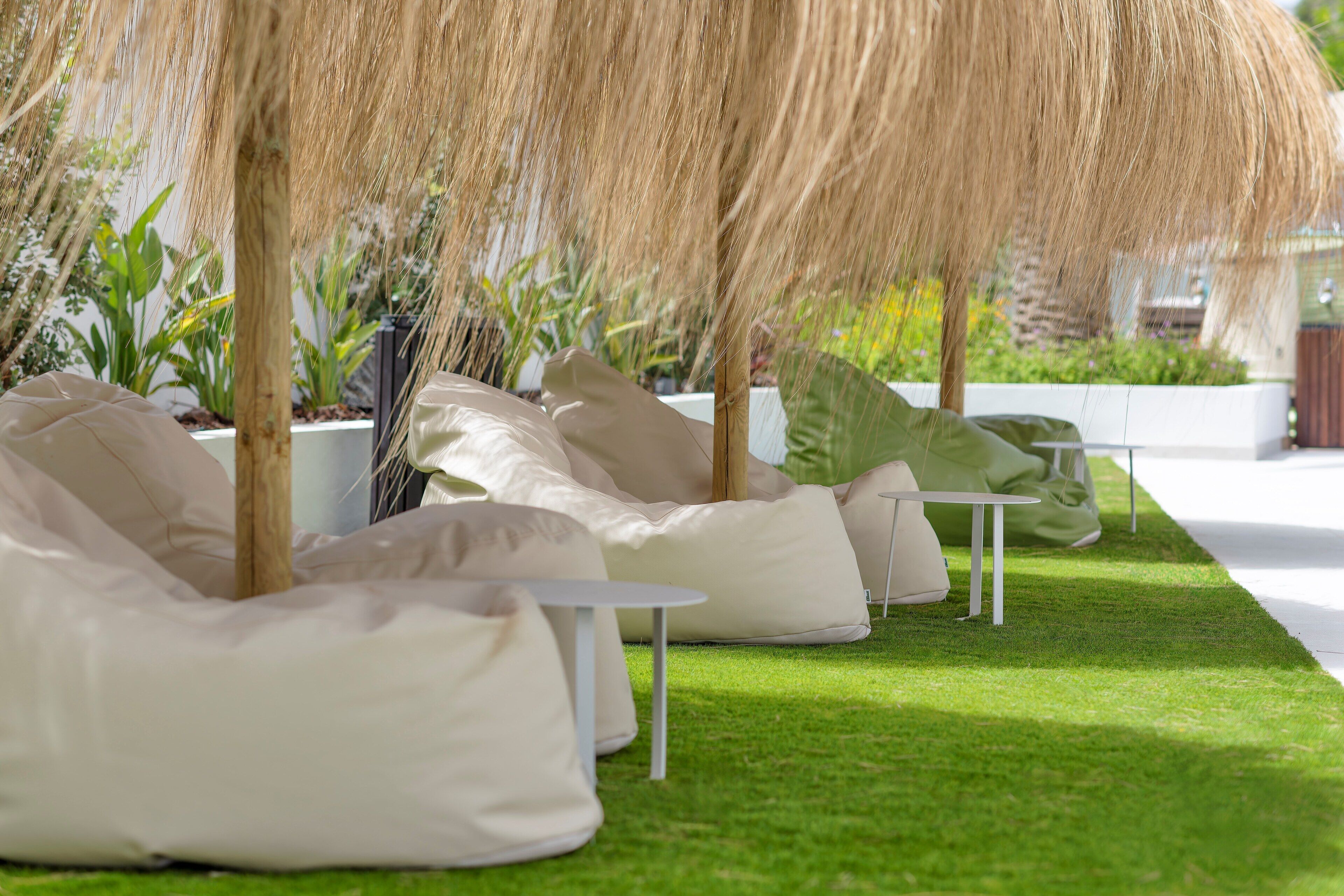 Outdoor seating with white tables and bean bags, surrounded by greenery and plants.