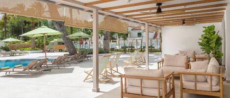 A poolside area with lounge chairs, a wooden pergola, and a seating area with cushions.