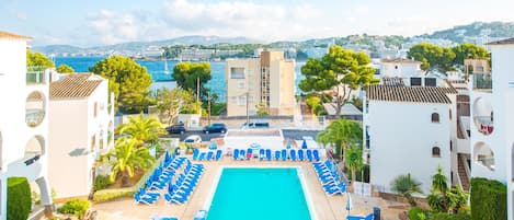 A pool area with blue lounge chairs and a clear view of the sea and hills in the background.