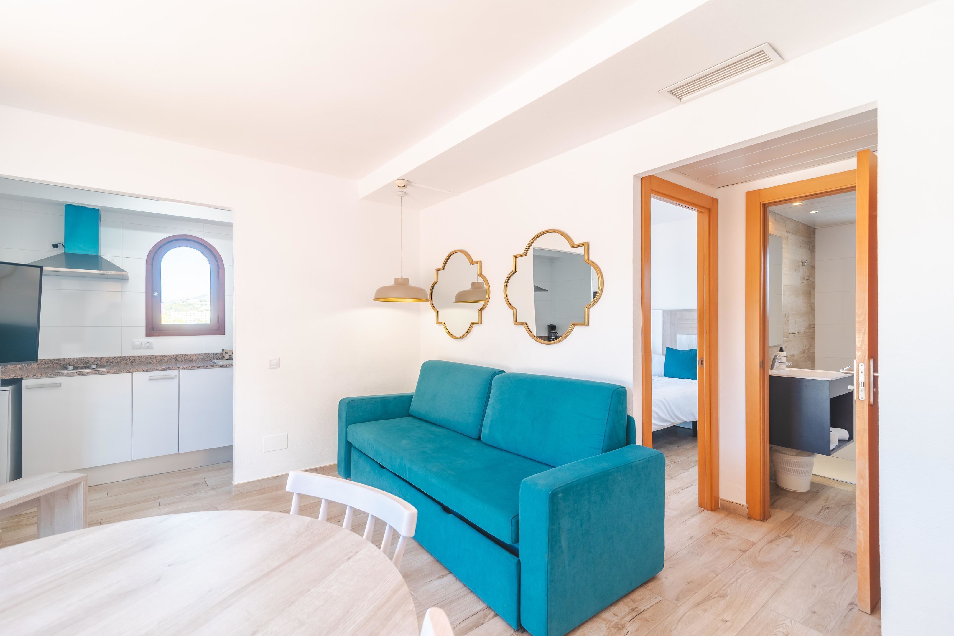 A modern apartment with a kitchen, a teal sofa, and a dining area.