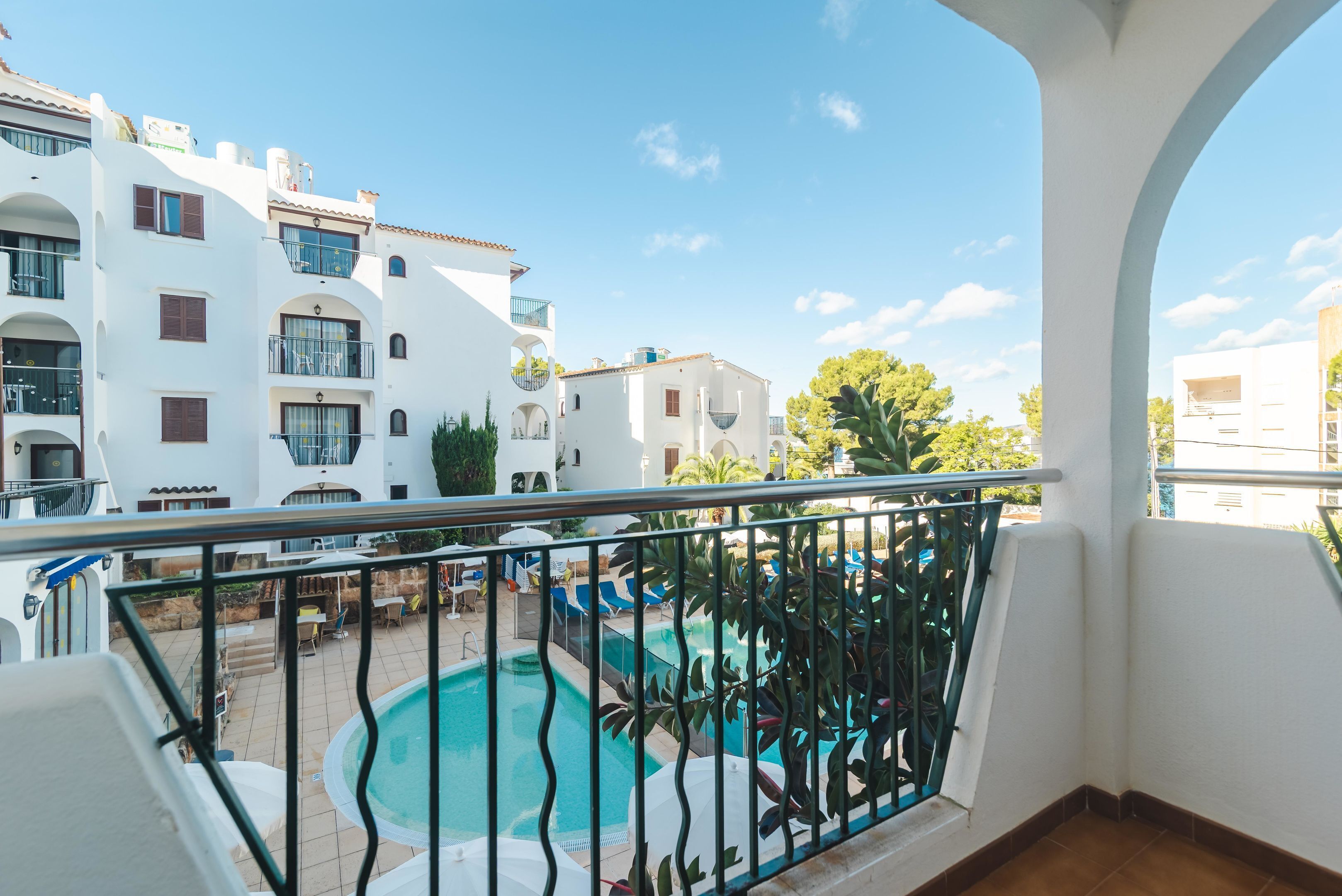 Uma varanda com vista para uma piscina, edifícios brancos e um céu limpo.