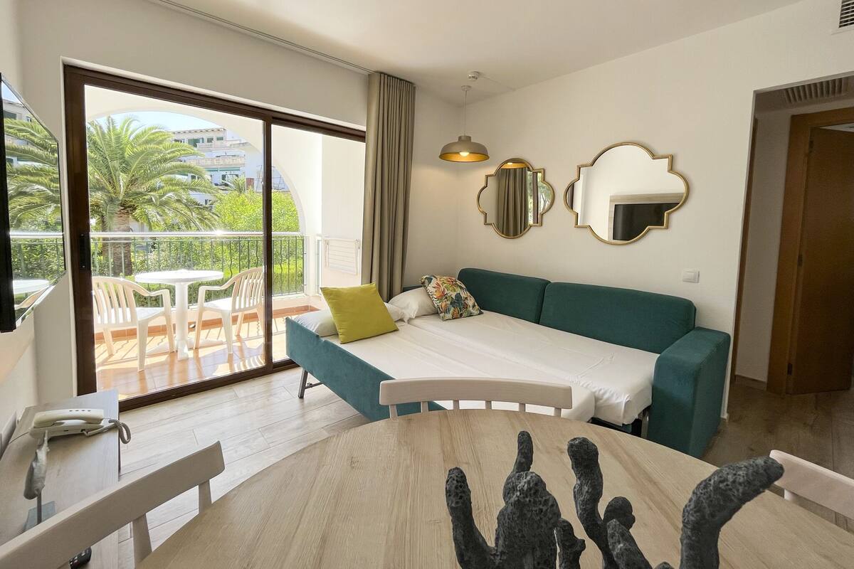 A modern hotel room with a balcony, a sofa, a dining table, and a phone on the side table.