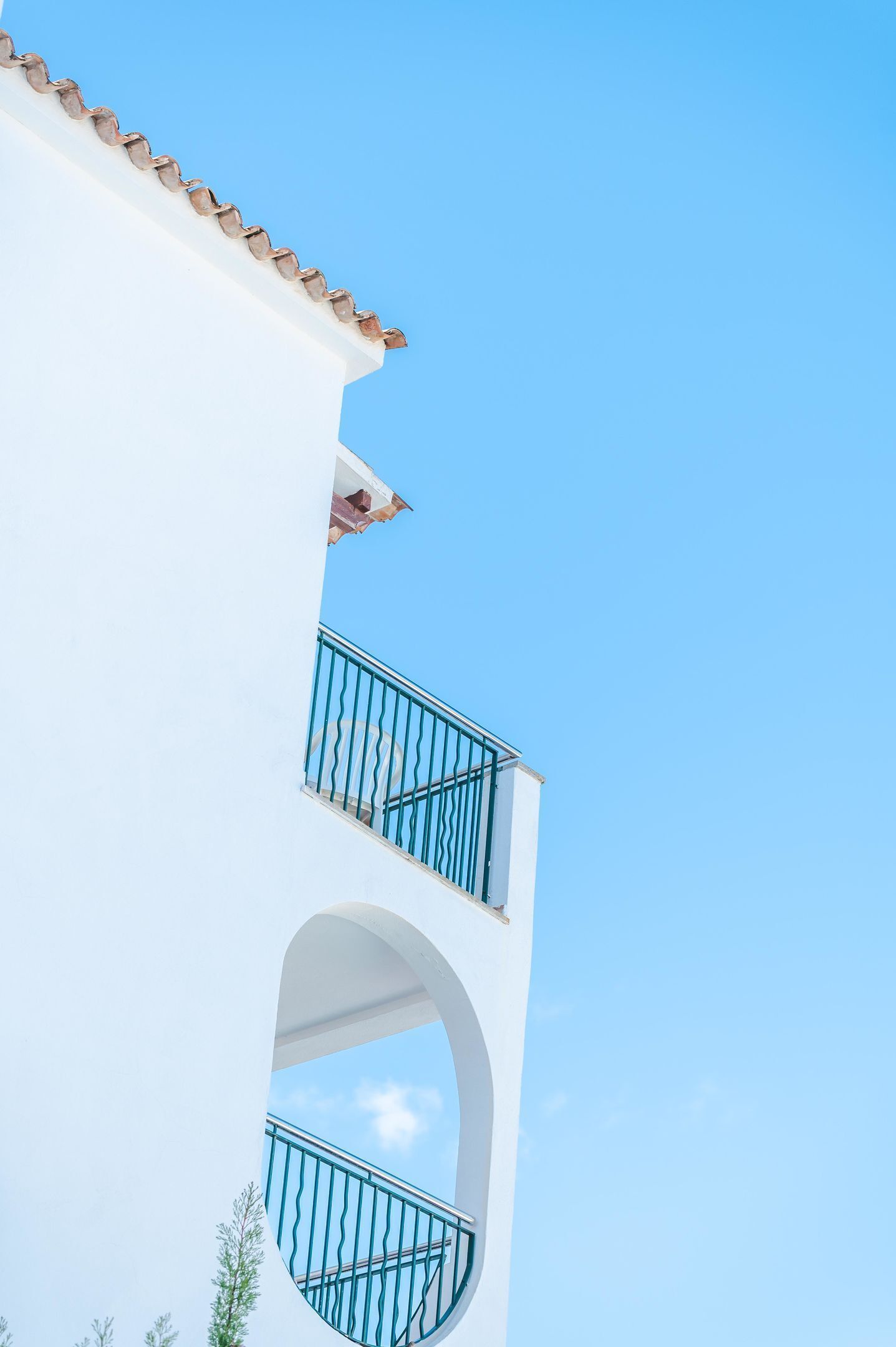 Ein weißes Gebäude mit blauem Balkon und einem wolkenlosen, blauen Himmel.