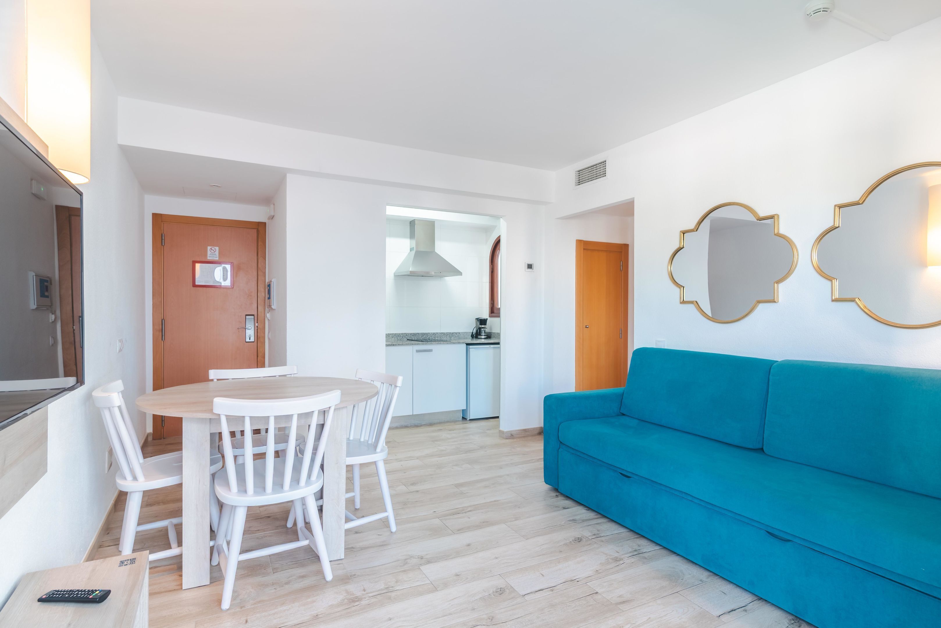 Ein modernes Wohnzimmer mit einem blauen Sofa, einem Esstisch mit Stühlen und einer Küche im Hintergrund.