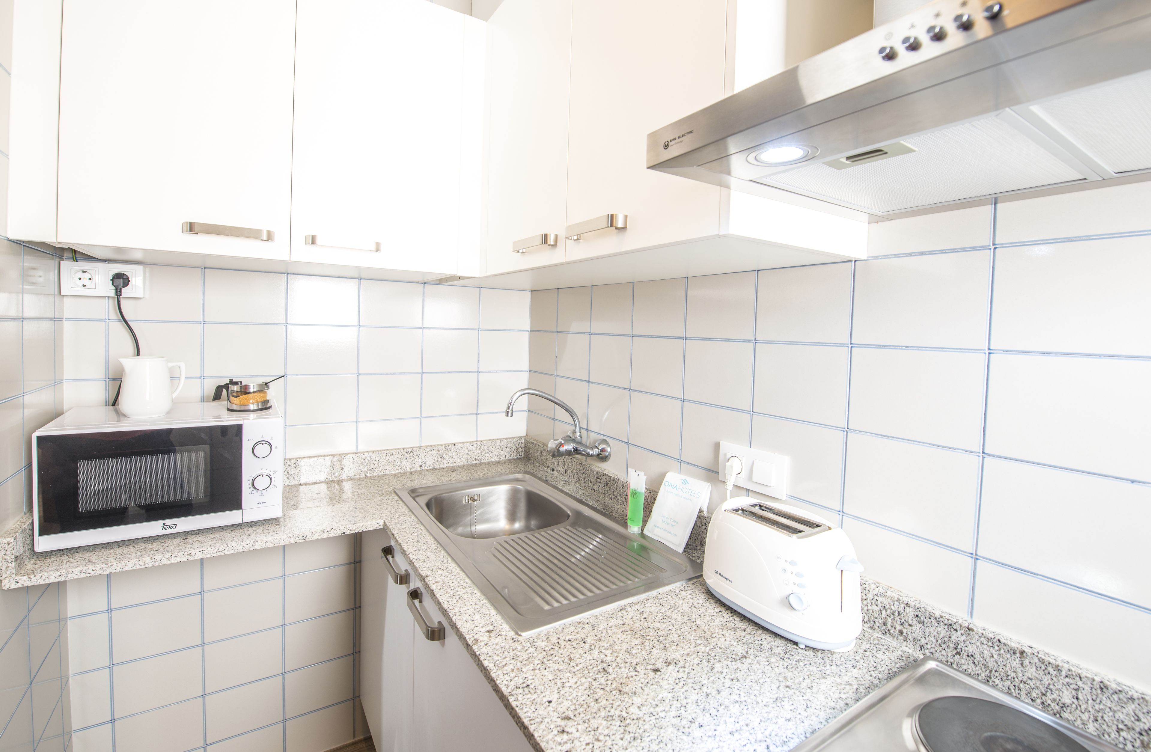 A modern kitchen with white cabinets, a stainless steel sink, a microwave, a toaster, and a kettle.
