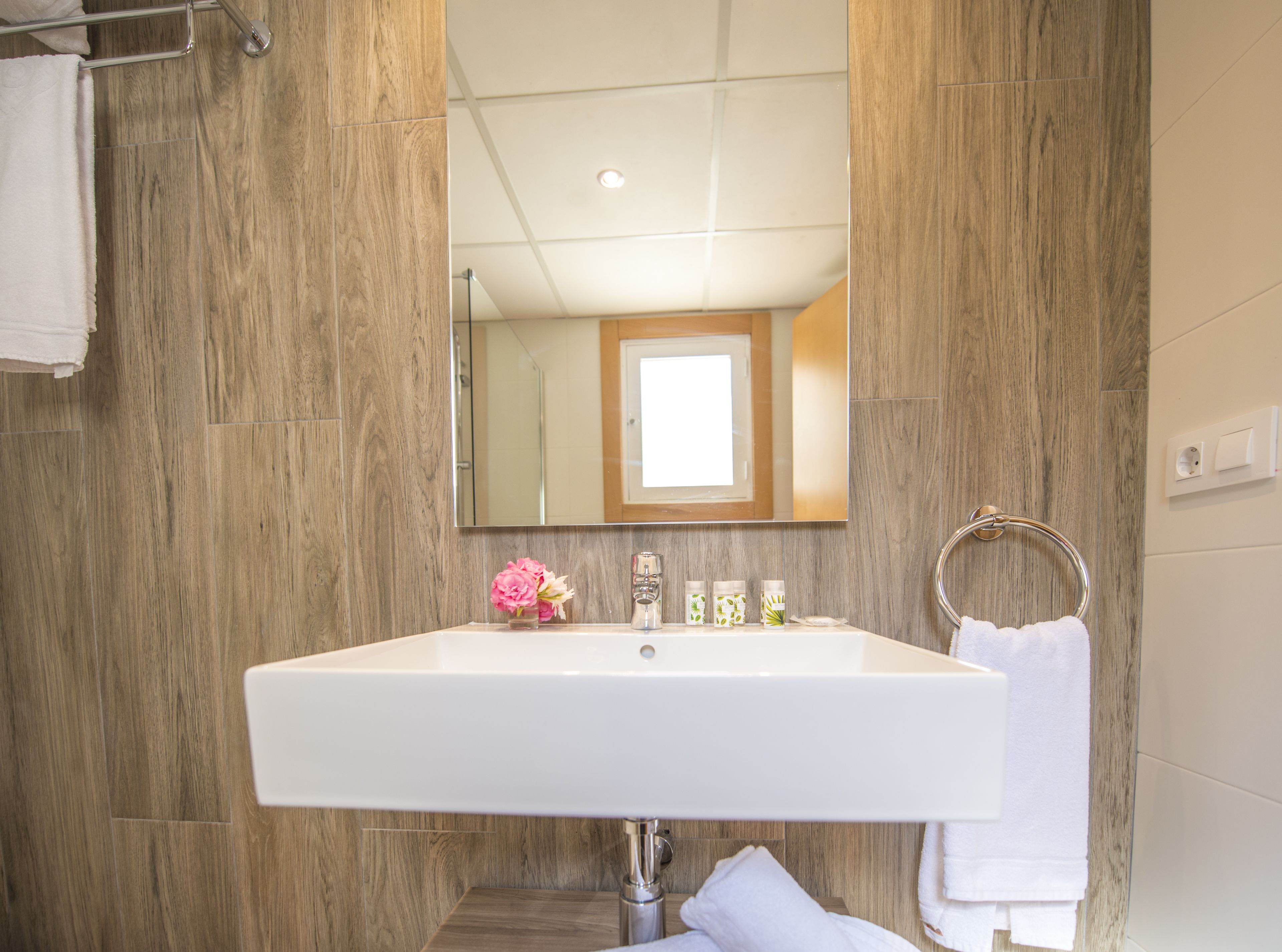 A bathroom with a large mirror, white sink, and wooden wall panels.