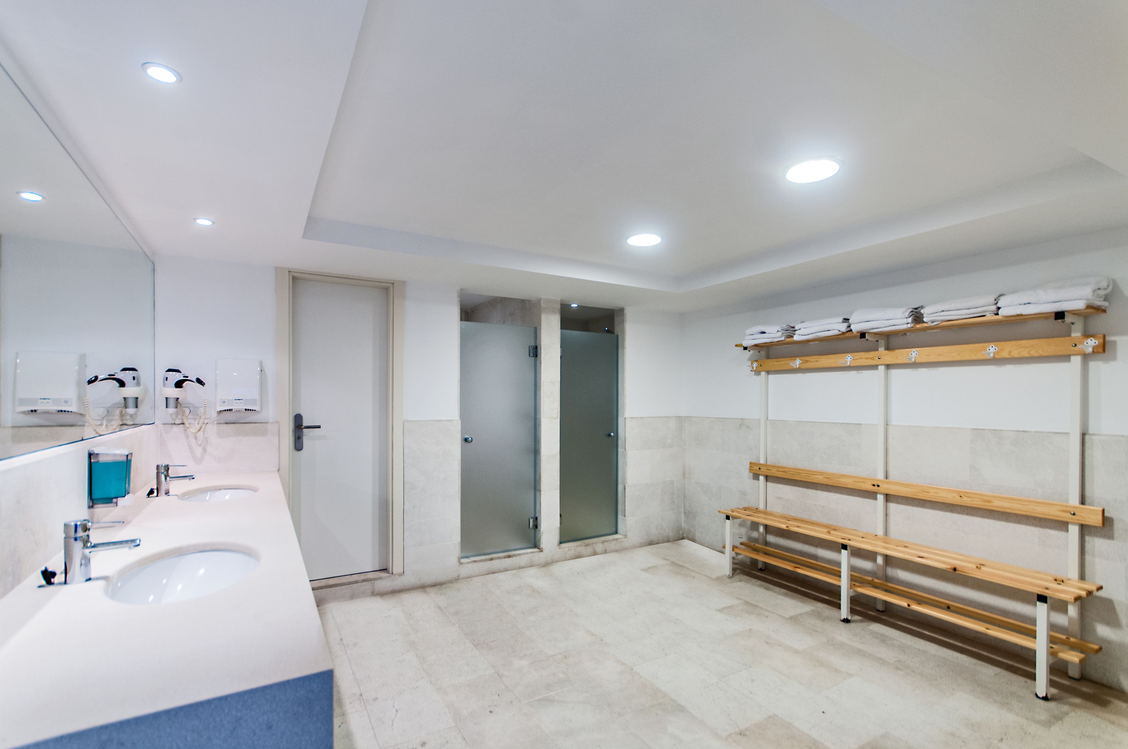 A modern bathroom with two sinks, a bench, and a towel rack.